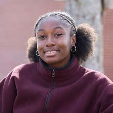 Smiling young woman with hair in puffs wearing hoop earrings and a burgundy zip-up jacket outdoors.